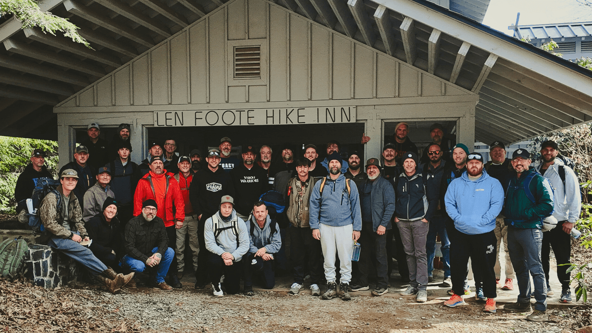 A large group of men from the Vision Warriors brotherhood posing together in front of the Len Foote Hike Inn